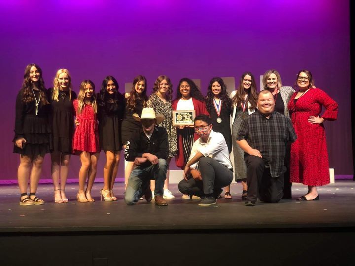 A group of high school students posed with a plaque on a theater stage