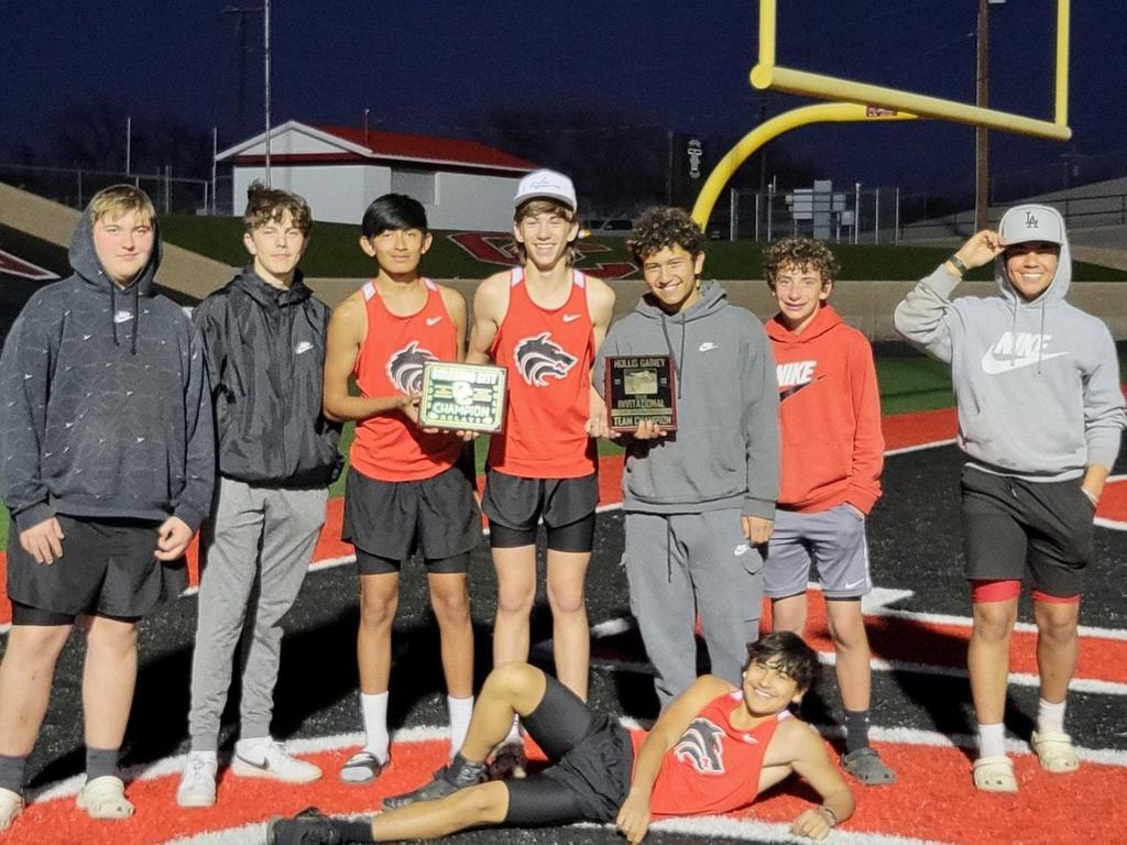 8 high school boys on the track team posing with plaques on the football field